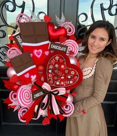 a woman standing in front of a door holding a heart shaped wreath with chocolates on it