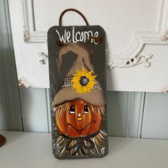 a welcome sign with a scarecrow hat and sunflowers on it, sitting next to a door