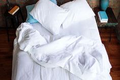 an unmade bed with white sheets and blue pillows on top of it in front of a brick wall