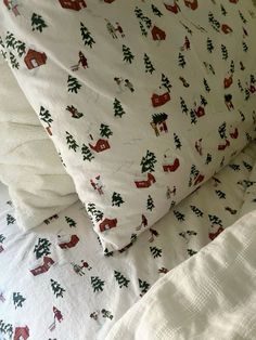 a bed with white sheets covered in christmas decorations and red houses on the pillow cases