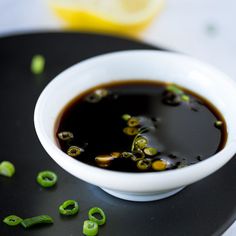 a white bowl filled with soup sitting on top of a black plate next to lemon wedges