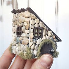 a small house made out of rocks and moss is held in the palm of a person's hand