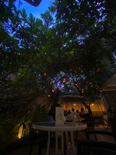 an orange tree is lit up at night with people sitting under it and tables in the foreground