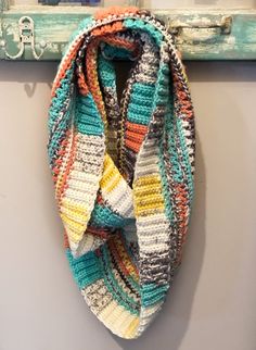 a multicolored crocheted scarf hanging from a hook on a white wall