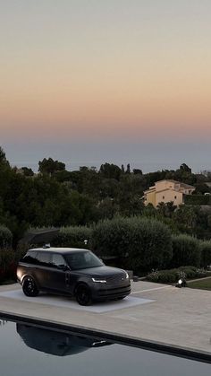 a black car is parked in front of a swimming pool at dusk with the sun going down