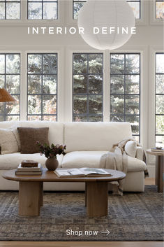 a living room with white couches and tables in front of large windows that look out onto the woods