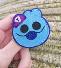 a hand holding a blue felt brooch with a smiley face