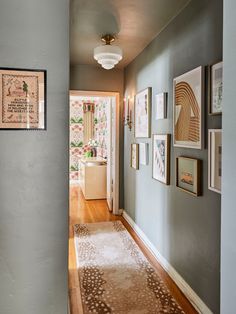 a hallway with pictures on the wall and a rug in front of it, next to a doorway