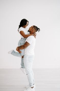 a man holding a woman on his back in the middle of an empty room with white walls