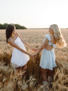 two young women holding hands in a wheat field