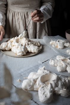 a woman in an apron is decorating some white frosted cookies on a table