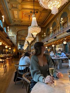 a woman sitting at a table with a glass of wine in her hand and chandelier hanging from the ceiling