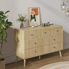 a wooden dresser sitting next to a potted plant and a painting on the wall