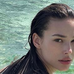 a woman with wet hair standing in the water looking off to the side, wearing a black swim suit