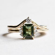 an engagement ring with a green stone surrounded by two diamond accents on the band, set in yellow gold and white gold