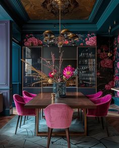 a dining room with blue walls, pink chairs and a wooden table in the center