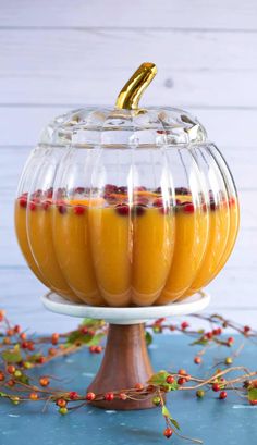 a glass container filled with oranges on top of a wooden stand next to berries