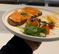 a person holding a white plate with food on it that includes eggs, tomatoes and other vegetables