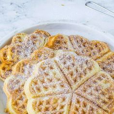 four waffles on a white plate covered in powdered sugar