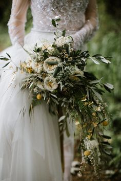 a bride holding a bouquet of flowers and greenery