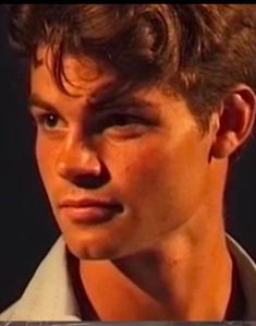 a close up of a young man wearing a white shirt and black collared shirt