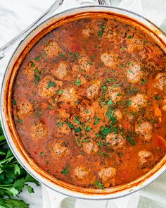 a large pot filled with meatballs and sauce on top of a white table cloth