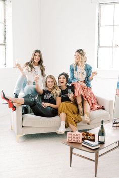 four women sitting on a couch posing for the camera with one woman holding a wine bottle