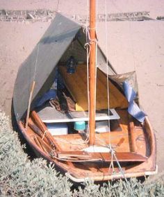 a small wooden sailboat sitting on the beach next to some bushes and sand,