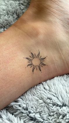 a small sun tattoo on the wrist is shown in black ink, and it appears to be tiny