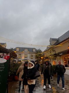 people walking down the street in front of shops on a rainy day with lights strung overhead