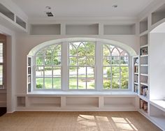 an empty living room with large windows and white furniture in the center, along with built - in bookshelves