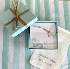 an open box with a necklace in it sitting on a striped tablecloth next to a card