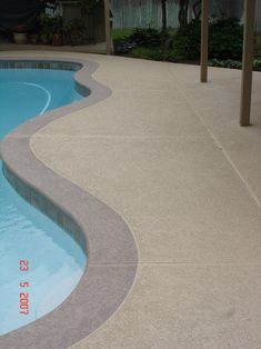 an empty swimming pool with concrete edgings and a pergolated walkway leading up to it