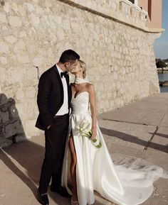 a man and woman in formal wear standing next to each other near a stone wall