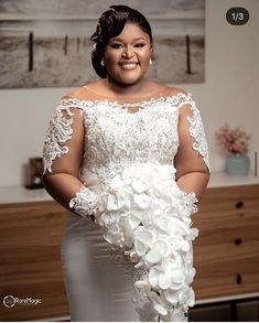 a woman in a white dress holding a bouquet of flowers and smiling at the camera