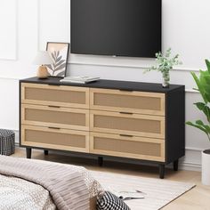 a flat screen tv sitting on top of a wooden dresser next to a bed and potted plant