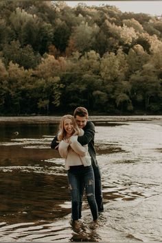 a man and woman are standing in the water near some trees with their arms around each other