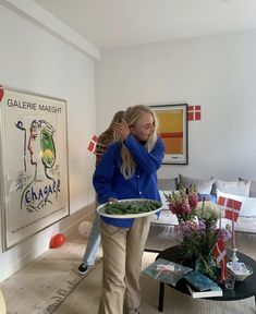 two women hug each other in the middle of a room with paintings on the wall