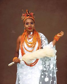 an african woman dressed in white and orange holding a large piece of fur on her arm