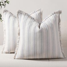 two blue and white striped pillows sitting on top of a couch next to a potted plant