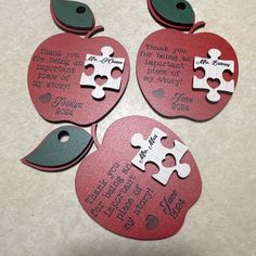 four pieces of red and green apple shaped tags with puzzle pieces attached to them, on a white surface