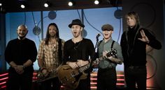 four men standing in front of a microphone and guitar