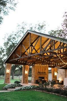 a covered patio with string lights on the roof and tables in the grass below it