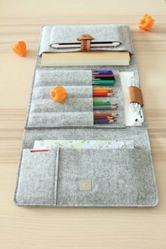 a gray felt case with pencils, pens and other items in it on a wooden table