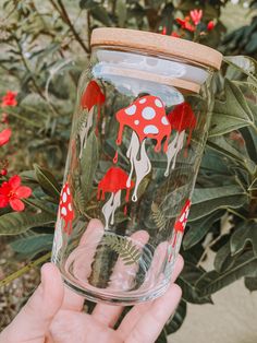 a hand holding up a glass with red and white designs on the bottom, in front of some flowers