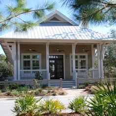 a small white house with porches on the front and side sides, surrounded by pine trees