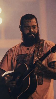 a man with a beard holding a guitar in front of a microphone and lights behind him