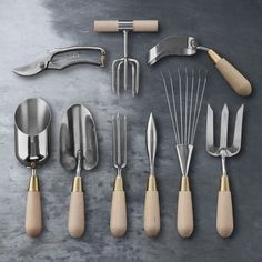 an assortment of kitchen utensils and tools on a gray surface with wooden handles