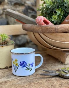 a white and blue coffee cup sitting on top of a wooden table next to a potted plant