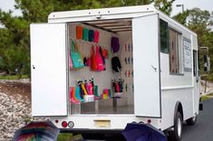 an open white truck with umbrellas and other items in the back door, on a road